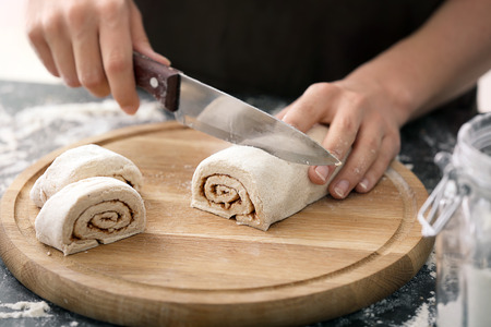 Woman cutting dough for cinnamon rolls on wooden boardの写真素材