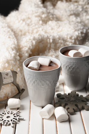 Cups of hot cocoa with marshmallows and Christmas decorations on wooden tableの写真素材