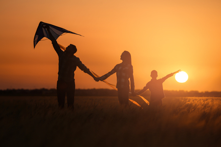 Happy family flying kite in the field at sunsetの写真素材