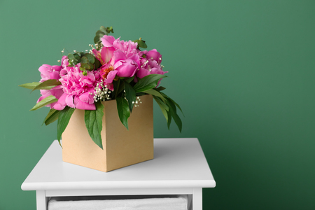 Box with beautiful peony flowers on table against color backgroundの写真素材