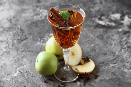 Glass of tasty drink with cinnamon and apple slices on grey textured backgroundの写真素材