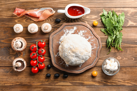 Composition with raw dough and ingredients for pizza on wooden backgroundの写真素材