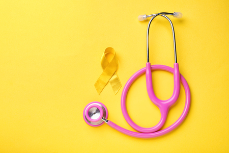 Yellow ribbon and stethoscope on color background. Cancer conceptの写真素材