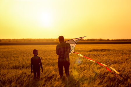 Happy father and son flying kite in the field at sunsetの写真素材