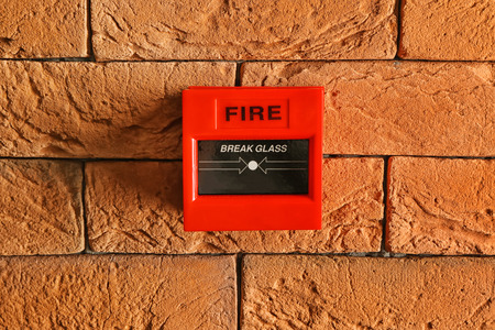 Modern fire call point on brick wall indoors