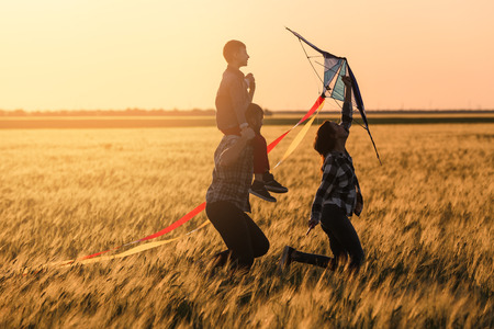 Happy family flying kite in the field at sunsetの写真素材