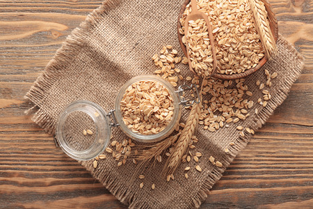 Glass jar with raw oatmeal flakes on wooden table
