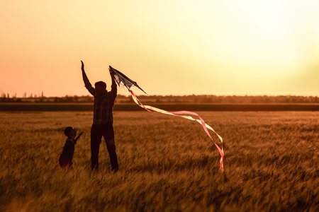 Happy father and son flying kite in the field at sunsetの写真素材