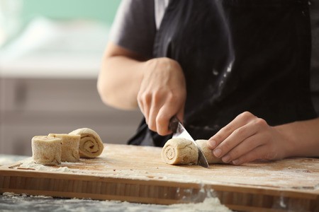 Woman cutting dough for cinnamon rolls on wooden boardの写真素材