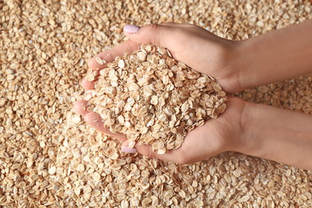 Woman with handful of raw oatmeal, closeup