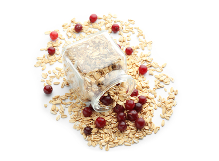 Overturned glass jar with raw oatmeal and cranberry on white backgroundの写真素材