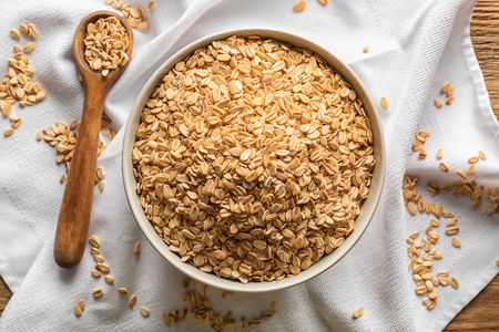 Bowl and spoon with raw oatmeal flakes on wooden table