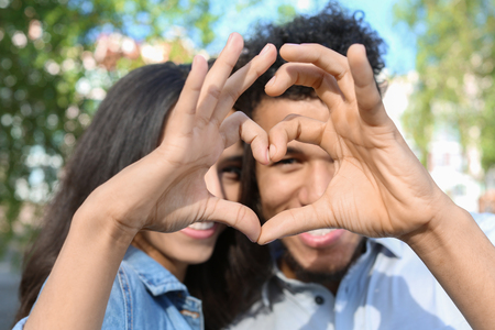 Happy African-American couple making heart with their hands in parkの写真素材