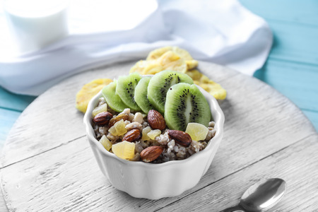 Bowl with tasty oatmeal, almonds, sliced kiwi and candied fruits on wooden tableの写真素材