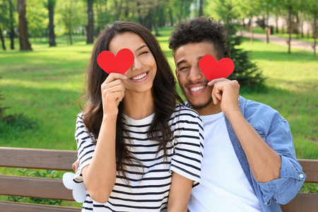 Happy African-American couple with paper hearts in park on spring dayの写真素材
