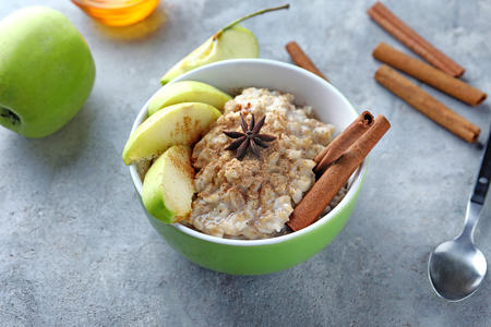 Bowl with tasty oatmeal, sliced apple and spices on grey textured backgroundの写真素材