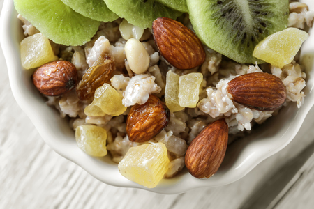 Tasty oatmeal with almonds, sliced kiwi and candied fruits in bowl on table, closeupの写真素材