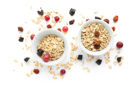 Bowls with raw oatmeal, raisins and cranberries on white backgroundの写真素材