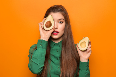 Beautiful young woman with avocado on color background