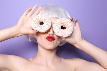 Young woman with wig and donuts on color backgroundの写真素材