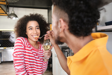 Young African-American man feeding his girlfriend in kitchen