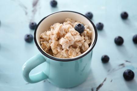 Cup with tasty oatmeal and blueberries on color background