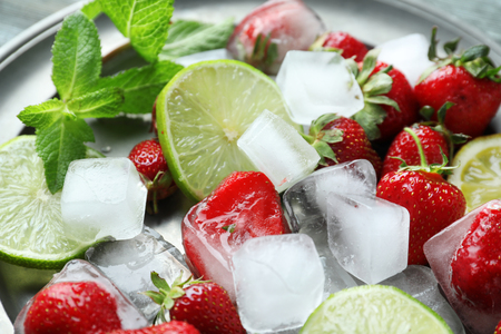 Plate with ice cubes, strawberries and citrus fruits on table, closeupの写真素材
