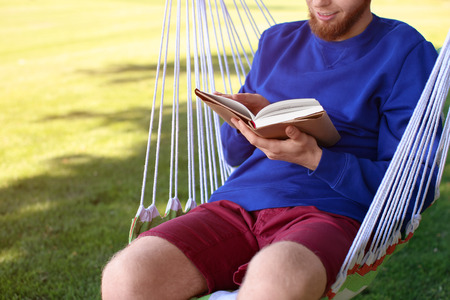 Young man reading book in hammock outdoorsの写真素材