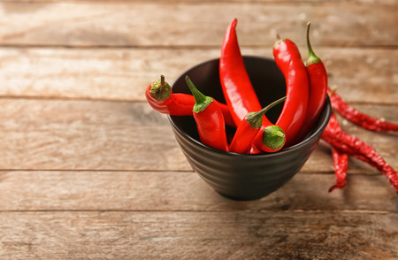 Bowl with fresh chili peppers on wooden background