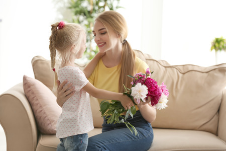 Cute little girl giving flowers to her mother at homeの写真素材
