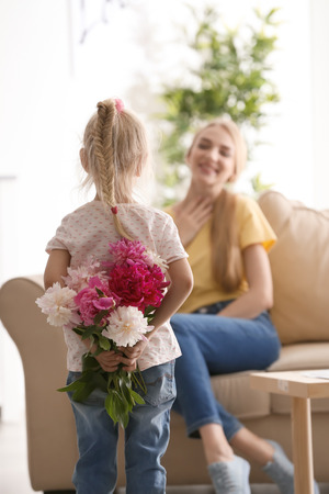 Cute little girl hiding bouquet of flowers for mother behind her backの写真素材