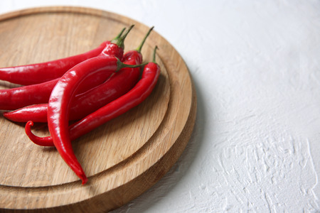 Wooden board with fresh chili peppers on light background