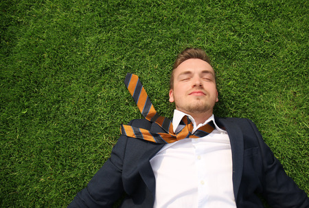 Young man in formal clothes relaxing on green grass outdoors