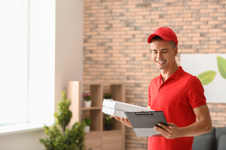 Young man with pizza boxes and clipboard indoors. Food delivery serviceの写真素材