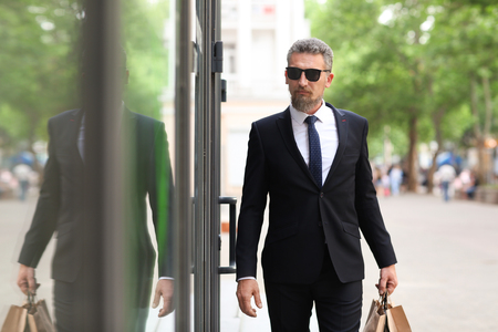 Handsome mature man in suit with shopping bags on city streetの写真素材