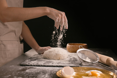 Woman sprinkling flour on dough against dark backgroundの写真素材