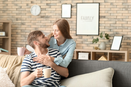 Happy young couple drinking hot coffee while resting at homeの写真素材