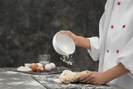 Chef sprinkling flour on dough in kitchenの写真素材