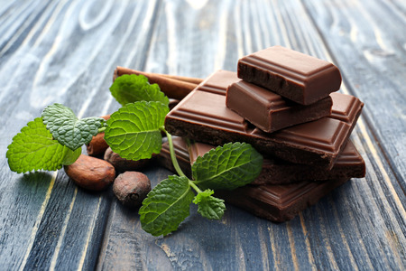 Pieces of tasty milk chocolate, mint and cocoa beans on wooden backgroundの写真素材