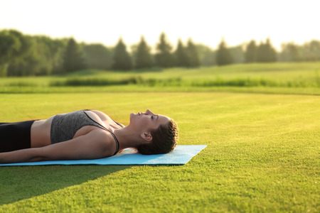Beautiful young woman lying on yoga mat outdoors in the morningの写真素材
