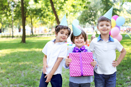 Cute little boy with gift box and his friends at birthday party outdoorsの写真素材