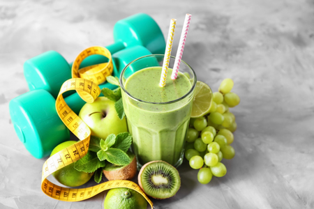 Glass of tasty smoothie, fresh fruits, measuring tape and dumbbells on table. Weight loss conceptの写真素材