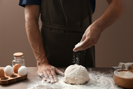 Man sprinkling dough with flour on color backgroundの写真素材