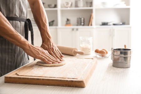 Professional chef with raw dough in kitchen
