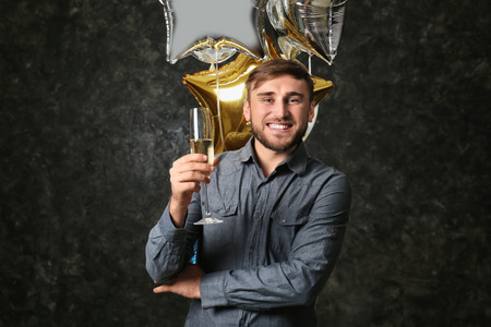 Young man with birthday balloons and glass of champagne on dark backgroundの写真素材