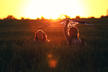 Cute little girls with kite in field at sunsetの写真素材