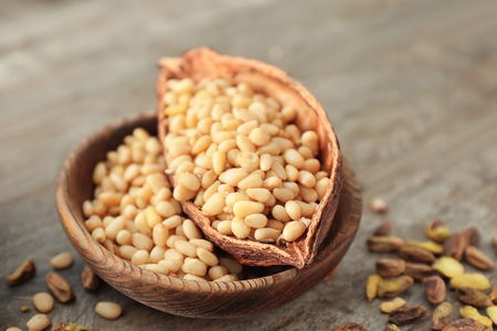 Bowl and cocoa pod with fresh tasty pine nuts on wooden tableの写真素材