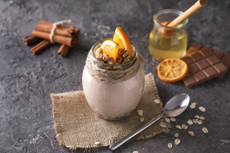 Tasty oatmeal dessert with sliced orange and walnuts in glass jar on grey backgroundの写真素材