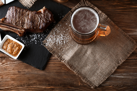 Mug of delicious beer with grilled steak on wooden tableの写真素材