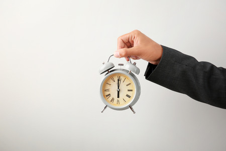 Businessman holding alarm clock on light background. Time management conceptの写真素材